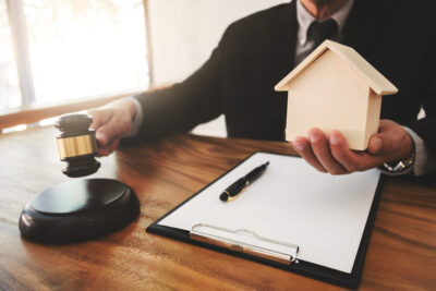 man holding gavel and tiny house in his hands while sitting at a desk