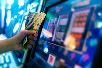 money in hand of gambler in front of slot machine